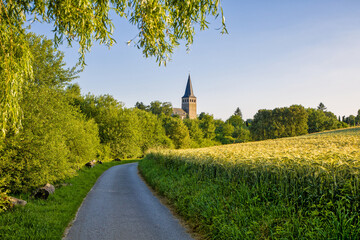 the catholic church of Ratingen Homberg at summer	evenig sun with blue sky and rye field and country path