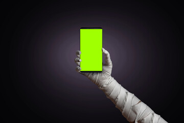 Mummy's hand wrapped in bandages holding blank sign template smartphone with empty copy space screen. Horrible risen dead mummy monster for a Halloween horror concept
