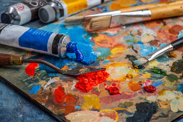 Old used brushes and palette knife in an artist's studio, palette with multi-colored spots of oil or acrylic paint, paint tubes