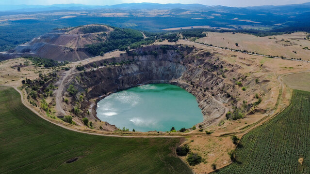 Aerial view of Tsar Asen Mine, Bulgaria &ndash; a former open-pit mine now filled with striking turquoise water. The steep terraced slopes and surrounding fields reflect the site's industrial past and natur