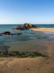 Fort National in Saint-Malo seen at low tide with sandy foreground and blue evening sky