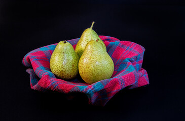 Three ripe pears rest elegantly in a bowl against a black background, highlighting their natural...