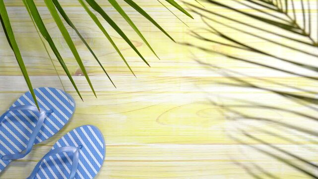 Blue flip-flops and palm leaf casting a shadow on yellow wooden planks, summer holiday concept