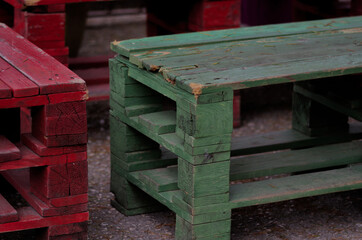 Close-up of reused wooden pallets painted in red and green, transformed into outdoor benches. The...