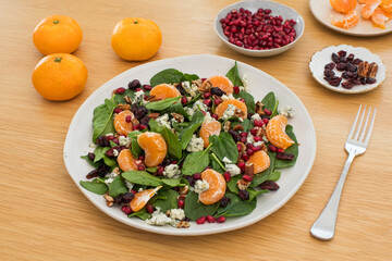 Fresh spinach salad with tangerines, pomegranate and cheese on wooden table