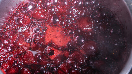 Cherry jam or sauce is cooked in a saucepan. Close-up. Background.