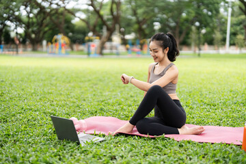 Yoga and Outdoor Fitness. Young woman practicing yoga at a park with a laptop for guidance.