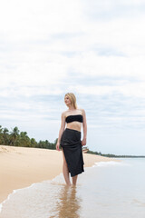 portrait of woman relaxing at summer resort, woman smiling on sandy beach, black bikini and skirt,...