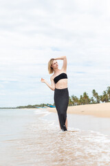 portrait of woman relaxing at summer resort, woman smiling on sandy beach, black bikini and skirt,...