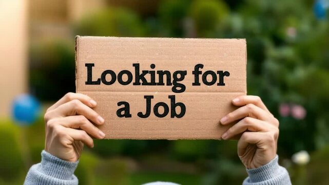 Person holding a cardboard sign indicating they are seeking employment.