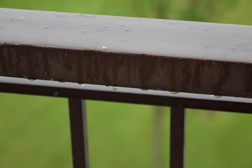 close-up macro raindrops dangling from brown painted iron railing