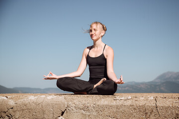 Woman practicing yoga in a serene outdoor setting, sitting cross-legged on a stone surface, embodying tranquility and mindfulness in nature