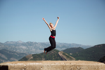 Joyful woman practicing yoga jump pose outdoors, surrounded by breathtaking mountain scenery,...