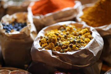 Colorful selection of dried herbs, spices, and natural ingredients in paper bags on rustic market...