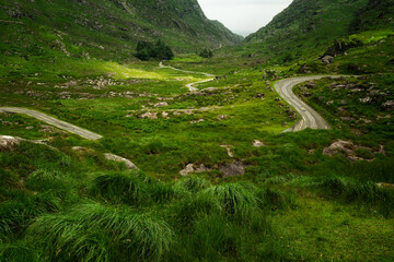A winding road meanders through rolling hills and towering mountains; a journey awaits.