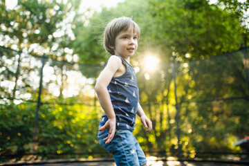 Cute boy jumping on a trampoline in a backyard on warm and sunny summer day. Sports and exercises...