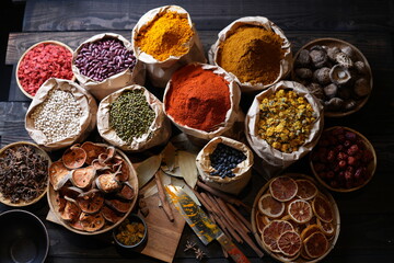 Colorful selection of dried herbs, spices, and natural ingredients in paper bags on rustic market table. Traditional Asian and herbal medicine concept.