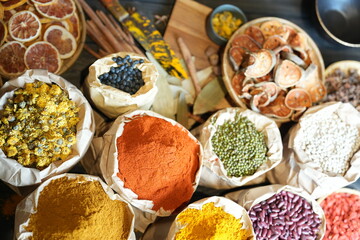 Colorful selection of dried herbs, spices, and natural ingredients in paper bags on rustic market table. Traditional Asian and herbal medicine concept.