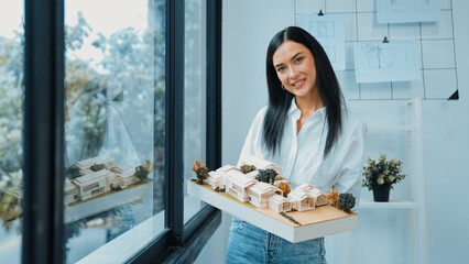 Close up of skilled young beautiful caucasian architect lift house model left side and right sight...