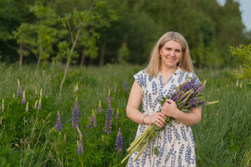 A beautiful woman in a summer dress looks into the camera, smiles, and holds a large bouquet of...