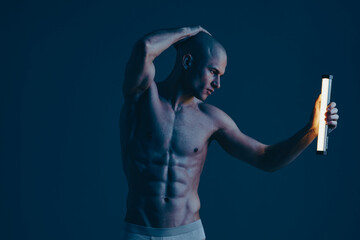 Athletic man posing dramatically with a light, showcasing his physique against a dark background....