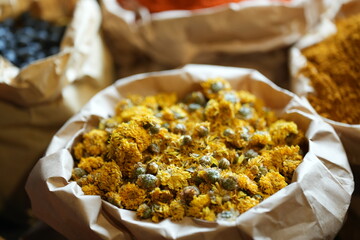 Colorful selection of dried herbs, spices, and natural ingredients in paper bags on rustic market table. Traditional Asian and herbal medicine concept.