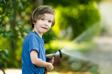 Cute little boy playing with garden hose on hot summer day. Child playing with water at summertime.