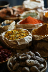 Colorful selection of dried herbs, spices, and natural ingredients in paper bags on rustic market table. Traditional Asian and herbal medicine concept.