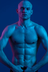 Fototapeta premium Athletic man with a confident expression, showcasing a strong physique against a blue background, highlighting the beauty of strength and determination.