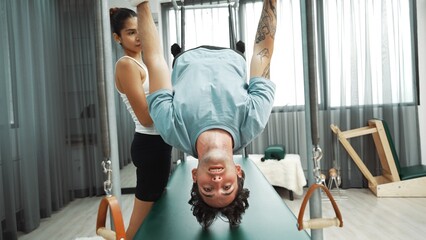 Healthy client practicing inverted leg raise on Pilates Cadillac under instructor guidance. Man...