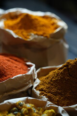 Colorful selection of dried herbs, spices, and natural ingredients in paper bags on rustic market table. Traditional Asian and herbal medicine concept.