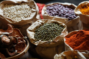 Colorful selection of dried herbs, spices, and natural ingredients in paper bags on rustic market table. Traditional Asian and herbal medicine concept.