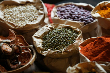 Colorful selection of dried herbs, spices, and natural ingredients in paper bags on rustic market table. Traditional Asian and herbal medicine concept.