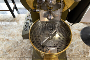 Close up of industrial coffee roaster with perforated drum and metal components.