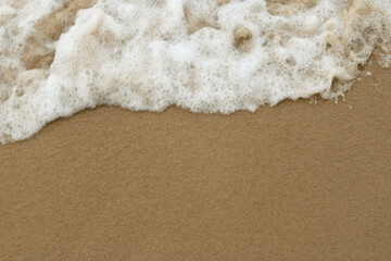 Gentle waves with white foam lap onto a smooth sandy beach.