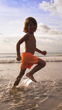 Small child running barefoot along sandy beach splashing water during golden hour evoking sense of freedom curiosity and outdoor exploration in beautiful natural coastal setting