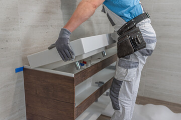 Installation of bathroom furniture. The plumber laying a double washbasin on a cabinet.
