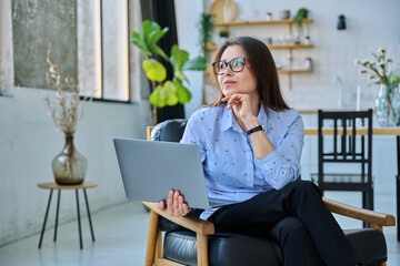Middle aged business woman sitting in chair with laptop computer