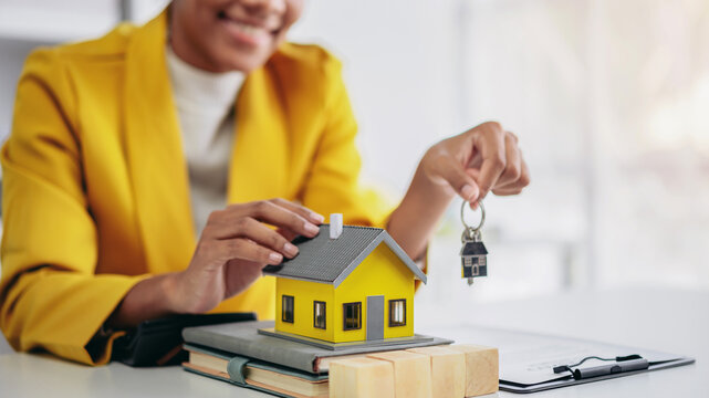 A woman is holding a key and yellow house. The house is a model and the woman is a real estate agent or a homeowner. Concept of loan and insurance