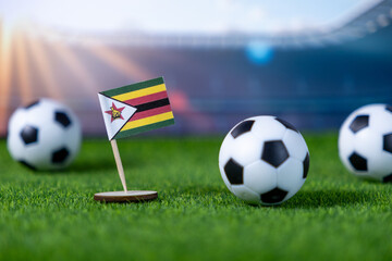 Zimbabwe flag stands on green grass with soccer balls, symbolizing national pride and participation in international football competitions and sports events