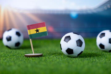 Ghana flag proudly stands on lush green artificial grass with soccer balls, symbolizing national team participation in global sports tournaments