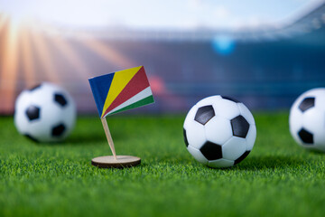 Seychelles flag with miniature soccer balls on green grass, set against a blurred stadium backdrop, symbolizing international football competition and national pride
