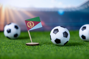 Miniature Eritrean flag stands proudly with soccer balls on vibrant green turf, symbolizing national team spirit in a global football stadium