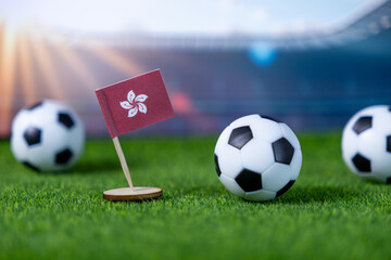 Miniature Hong Kong flag and classic soccer balls on vibrant green stadium grass, representing...