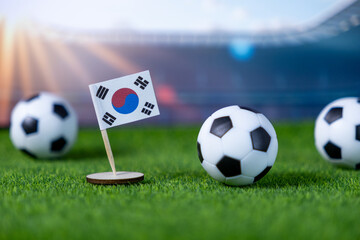 South Korean flag miniature stand with soccer balls on green artificial grass, symbolizing international sports competition and national team pride in a stadium atmosphere