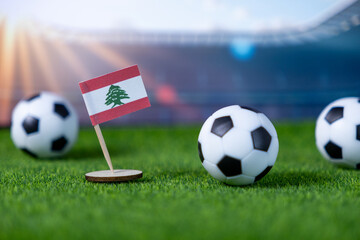 Miniature Lebanese flag on green soccer field with multiple footballs and stadium background, symbolizing national team sports competition and global championship event
