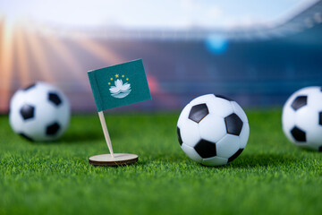 Macau SAR flag stands proudly on a green miniature football pitch with classic soccer balls, symbolizing global sports and national athletic competition