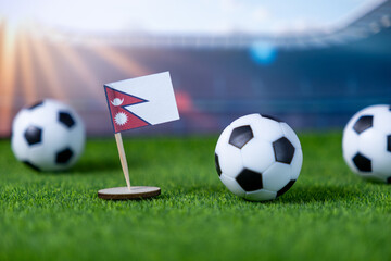 Small Nepali flag proudly stands with soccer balls on a bright green grass field, representing international football tournaments and national sports passion