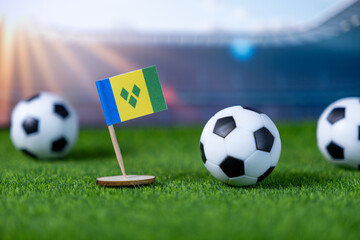 Miniature flag of Saint Vincent and the Grenadines with footballs on green artificial grass, symbolizing national team sports and international competition in a stadium