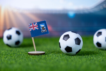 Small Falkland Islands flag positioned alongside miniature soccer balls on vibrant green grass,...